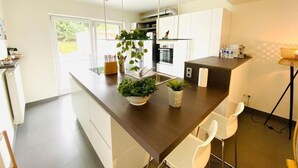 Une cuisine moderne dotée d’un îlot central, de meubles blancs et d’une plante suspendue.