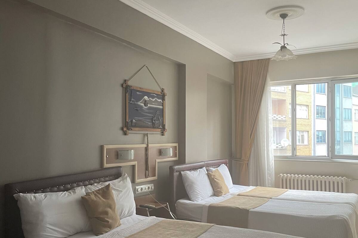 Habitación de hotel con dos camas, un cuadro en la pared, una ventana con cortinas y un radiador.