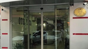 Entrada de hotel com porta de vidro, plantas em vasos e uma placa com a inscrição "YALTA HOTEL".