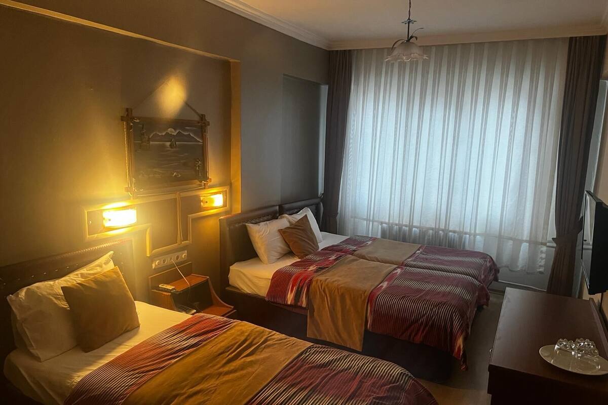 Habitación de hotel con dos camas, una mesita de noche, un escritorio, un televisor y una ventana con cortinas.