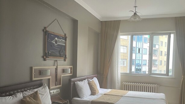 Quarto de hotel com duas camas, um ventilador de teto, uma janela com cortinas e um quadro pendurado na parede.