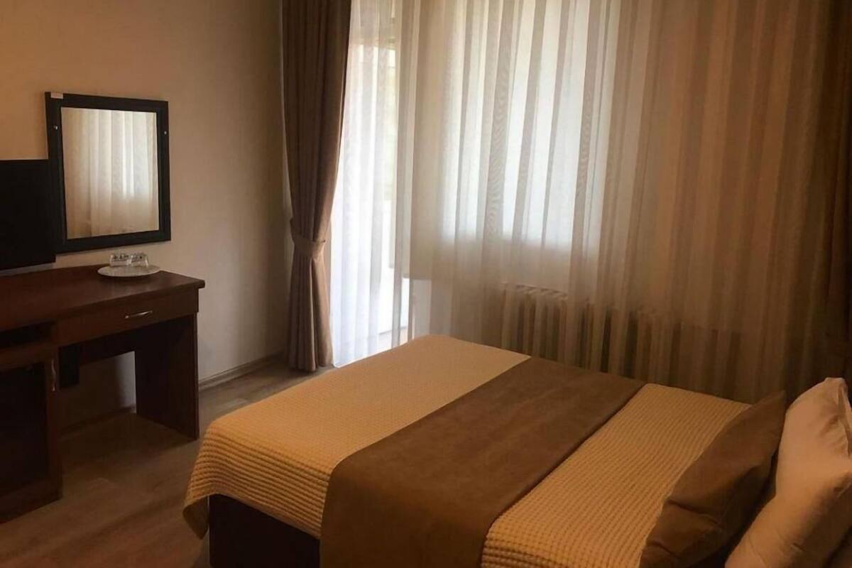 Habitación de hotel con cama, escritorio con televisor y ventana con cortinas.