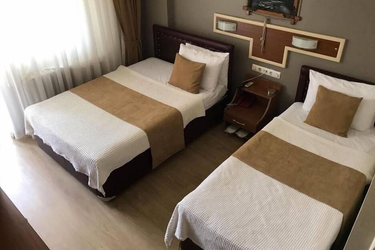 Habitación de hotel con dos camas, cada una con cabecero marrón, ropa de cama blanca y una mesita de noche con lámpara.