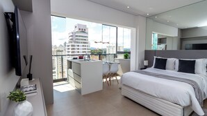 Une chambre moderne avec un grand lit, une petite kitchenette et un balcon offrant une vue sur la ville.