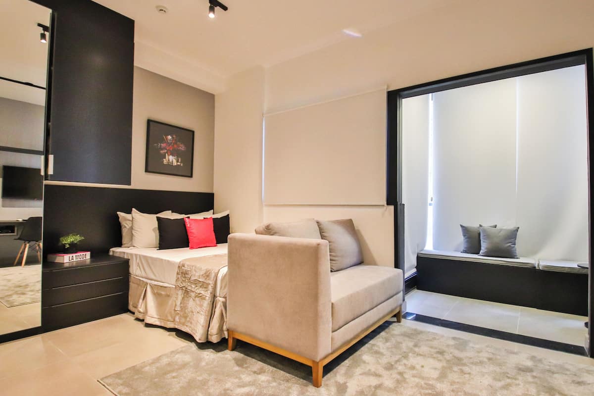 Un dormitorio moderno con cama, sofá, mesita de noche y un amplio ventanal.