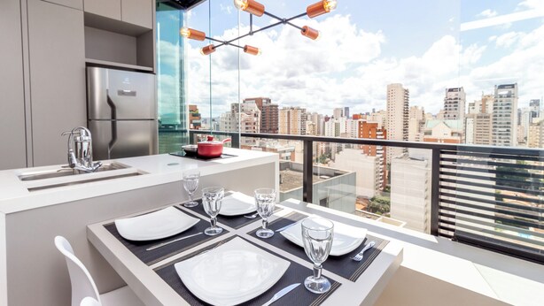 Une cuisine moderne dotée d’un grand îlot central, d’un coin repas avec une table pour quatre personnes et offrant une vue sur la ville grâce à de grandes fenêtres.