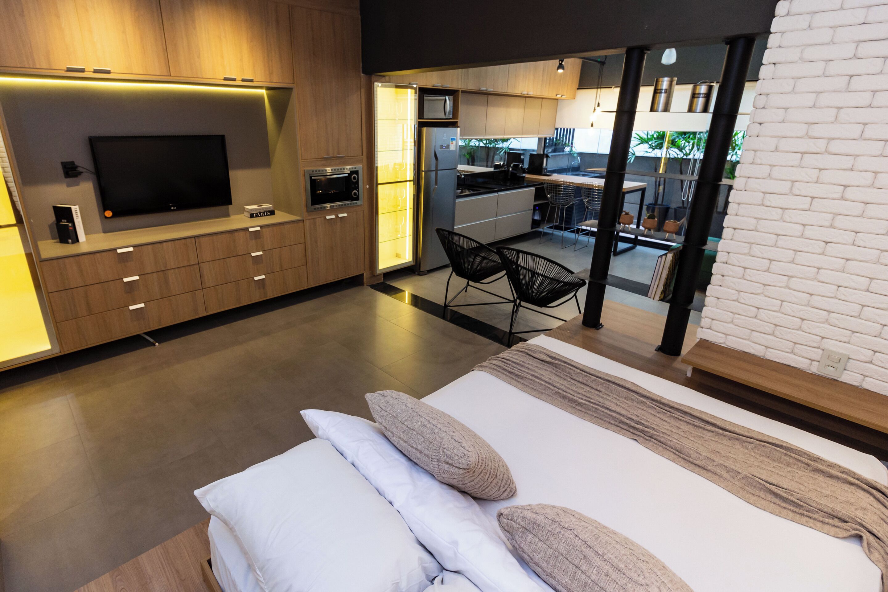 Un dormitorio moderno con una cama grande, televisión y una kitchenette al fondo.
