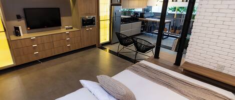 Un dormitorio moderno con una cama grande, televisión y una kitchenette al fondo.