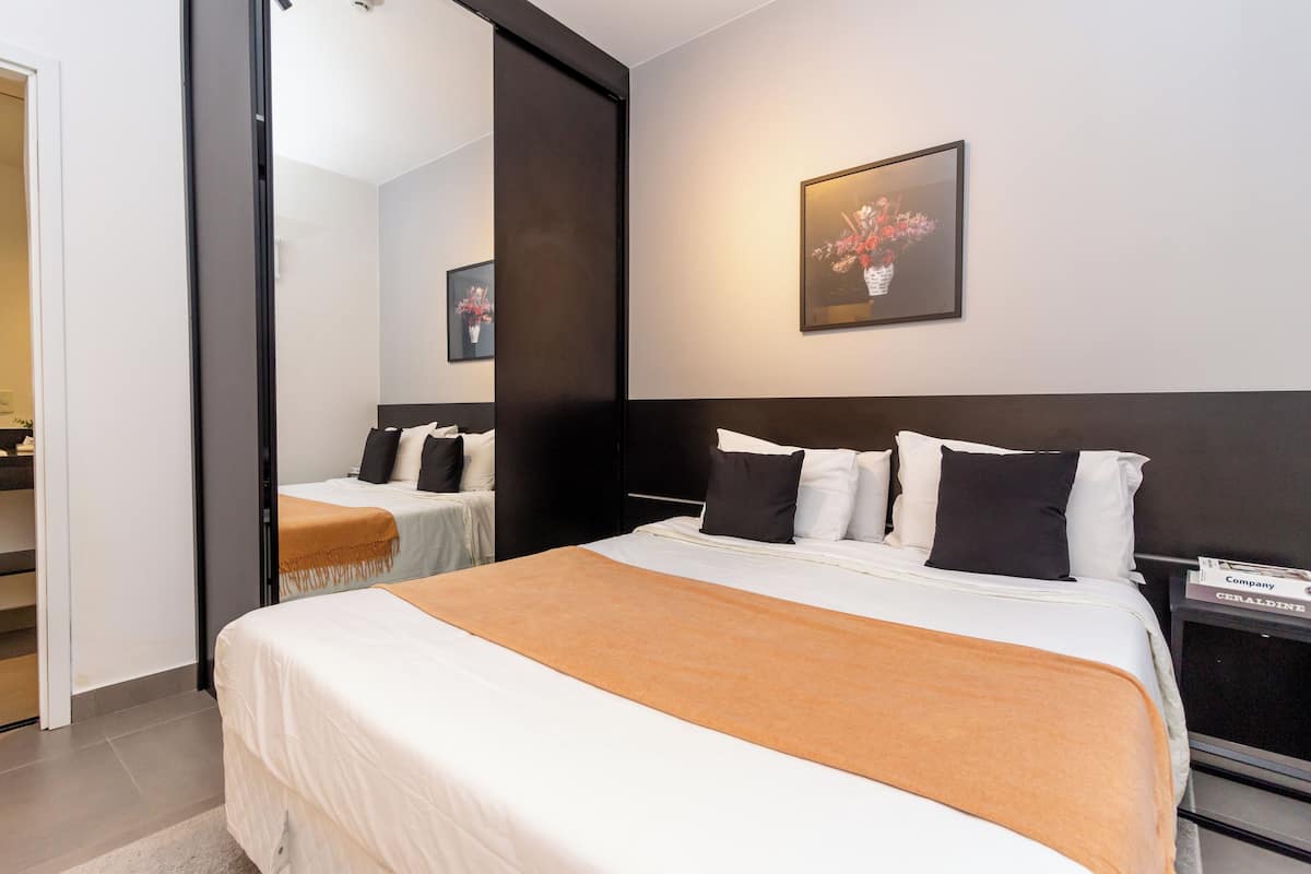 Un cuarto de hotel con una cama grande, una mesita de noche, un espejo y un cuadro en la pared.