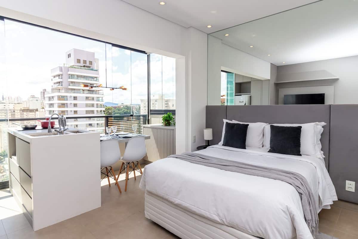 Un dormitorio moderno con una cama grande, un escritorio pequeño y un balcón con vista a la ciudad.