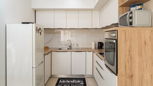 Una cucina moderna con mobili bianchi, un piano di lavoro in legno, un forno a microonde, un forno e un frigorifero.