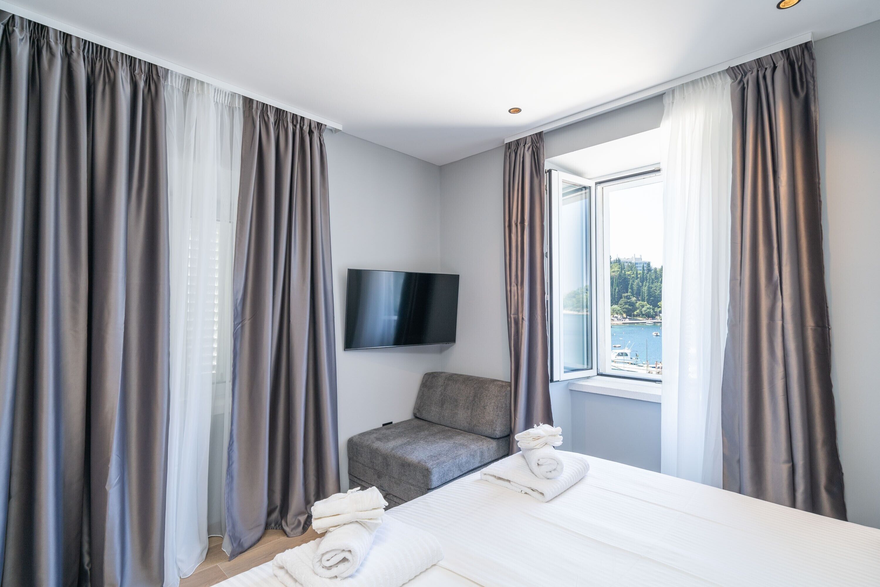 Et hotelværelse med seng, fjernsyn, stol og et vindue med gardiner.