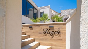 A staircase with wooden steps leading to a modern building with a large window and a stone wall in the background. - Apartments Villa Royale - Deluxe One Bedroom Apartment with Sea View (Cavtat)