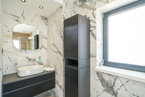 Ein modernes Badezimmer mit Marmorwand, einem großen Spiegel, einem integrierten Waschbecken und einem Fenster.