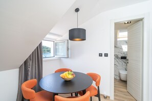 A dining area with a round table, orange chairs, a bowl of fruit, and a pendant light. - Apartments Villa Royale - One Bedroom Apartment with Sea View (Cavtat)