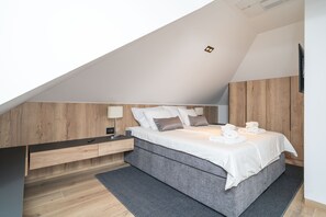 A modern bedroom with a sloped ceiling, wooden panel walls, a grey bed, and a small bedside table with a lamp. - Apartments Villa Royale - One Bedroom Apartment with Sea View (Cavtat)