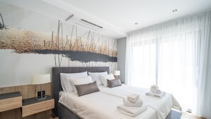 Ein modernes Hotelzimmer mit einem großen Bett, einem Nachttisch, einem Wandbild und einem Fenster mit transparenten Vorhängen.