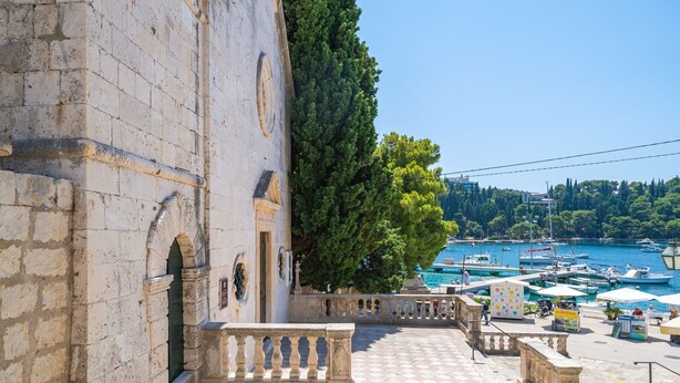 Ein Steinhaus mit einer Treppe, die zu einer Terrasse mit Blick auf einen Yachthafen und Boote führt.
