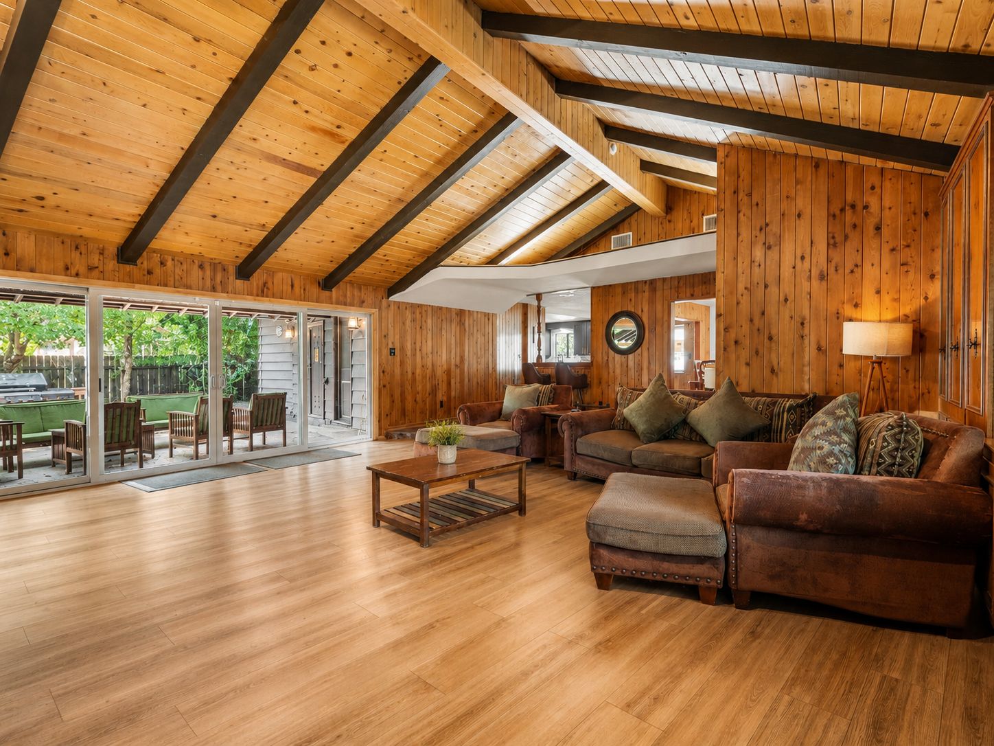 Amplia sala de estar con piso de madera, un gran sofá y un amplio ventanal corredizo que da a un patio exterior.