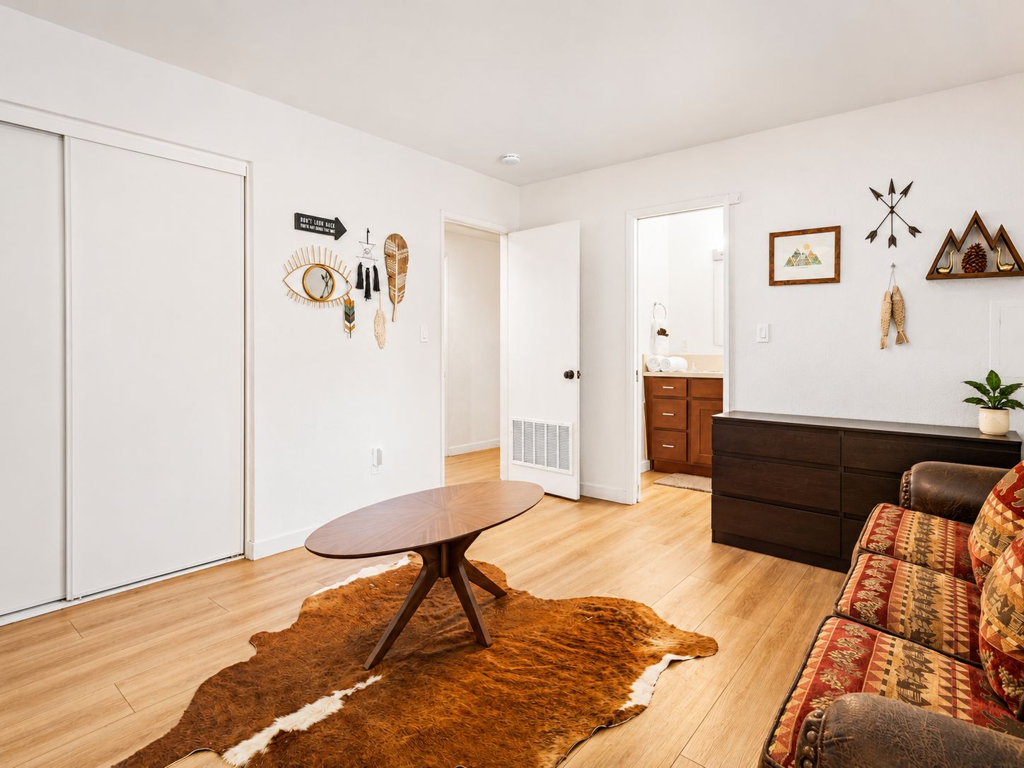 A modern living room with a wooden floor, a round table, a brown leather sofa, and a cowhide rug.