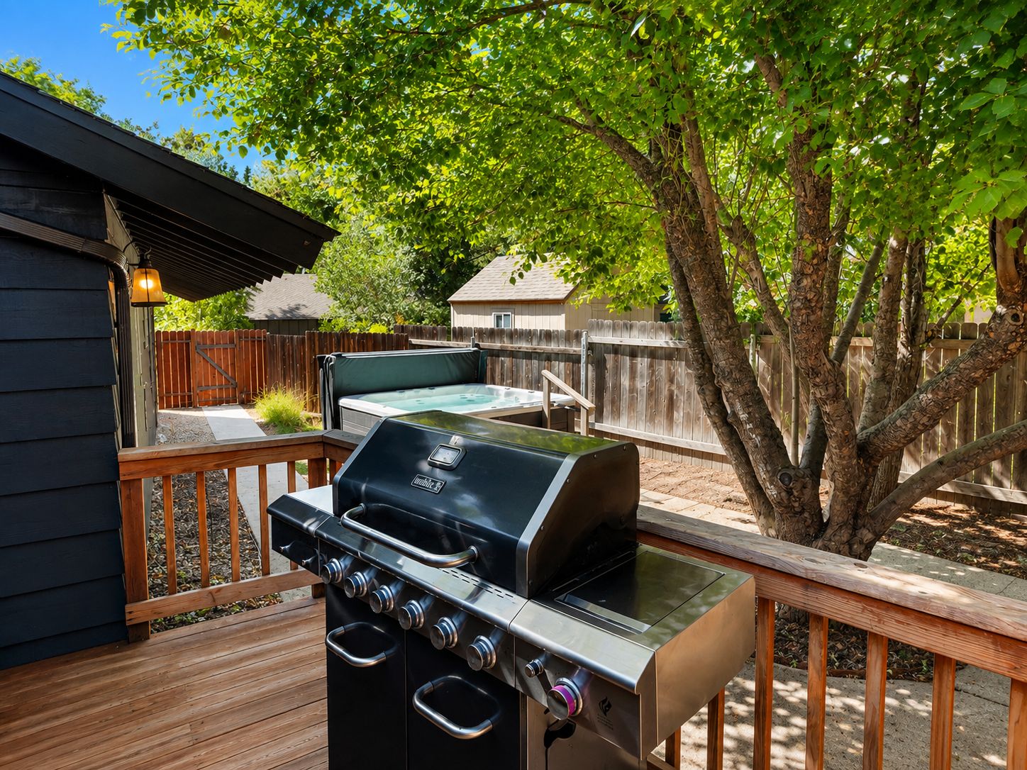 A backyard with a barbecue grill, a hot tub, and a wooden deck.