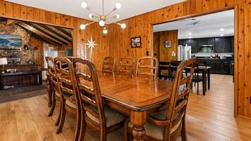 A dining area with a wooden table and chairs, a stone fireplace, and a kitchen visible through an open doorway.