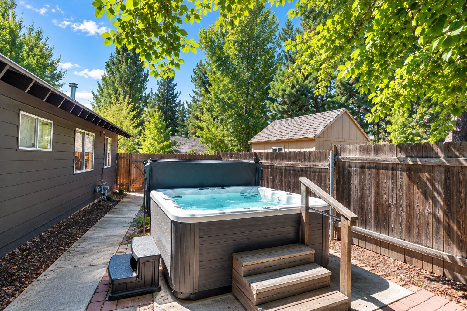A backyard with a hot tub, wooden steps, a fence, and a house.