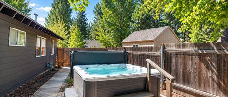 A backyard with a hot tub, wooden steps, a fence, and a house.