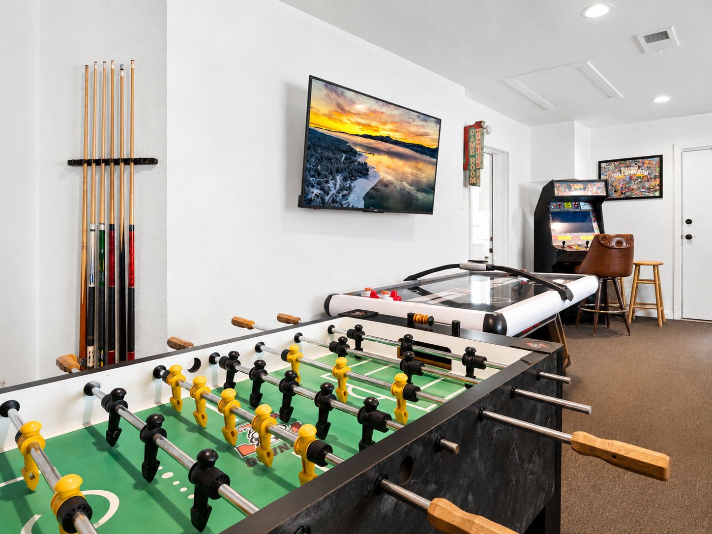A room with a foosball table, a pool table, and a mounted television.