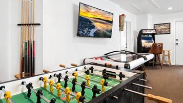 A room with a foosball table, a pool table, and a mounted television.