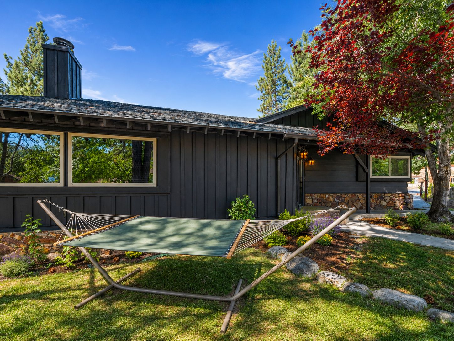 A house with a dark exterior, a chimney, and a hammock in the yard.