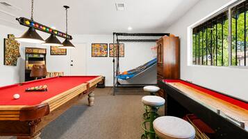 A pool table with a red felt surface, a hanging lamp, and a pool cue.