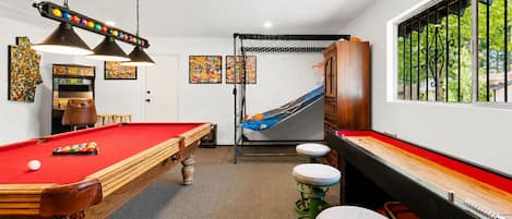 A pool table with a red felt surface, a hanging lamp, and a pool cue.
