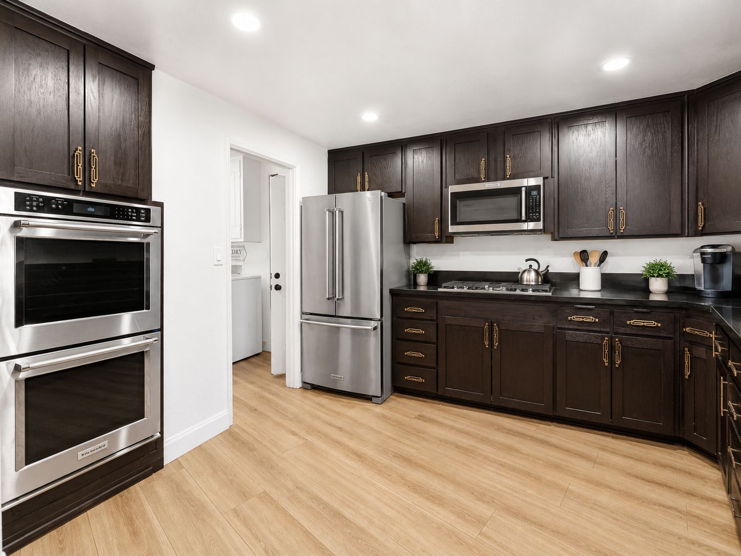 A modern kitchen with dark wood cabinets, stainless steel appliances, and a wooden floor.