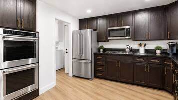 A modern kitchen with dark wood cabinets, stainless steel appliances, and a wooden floor.