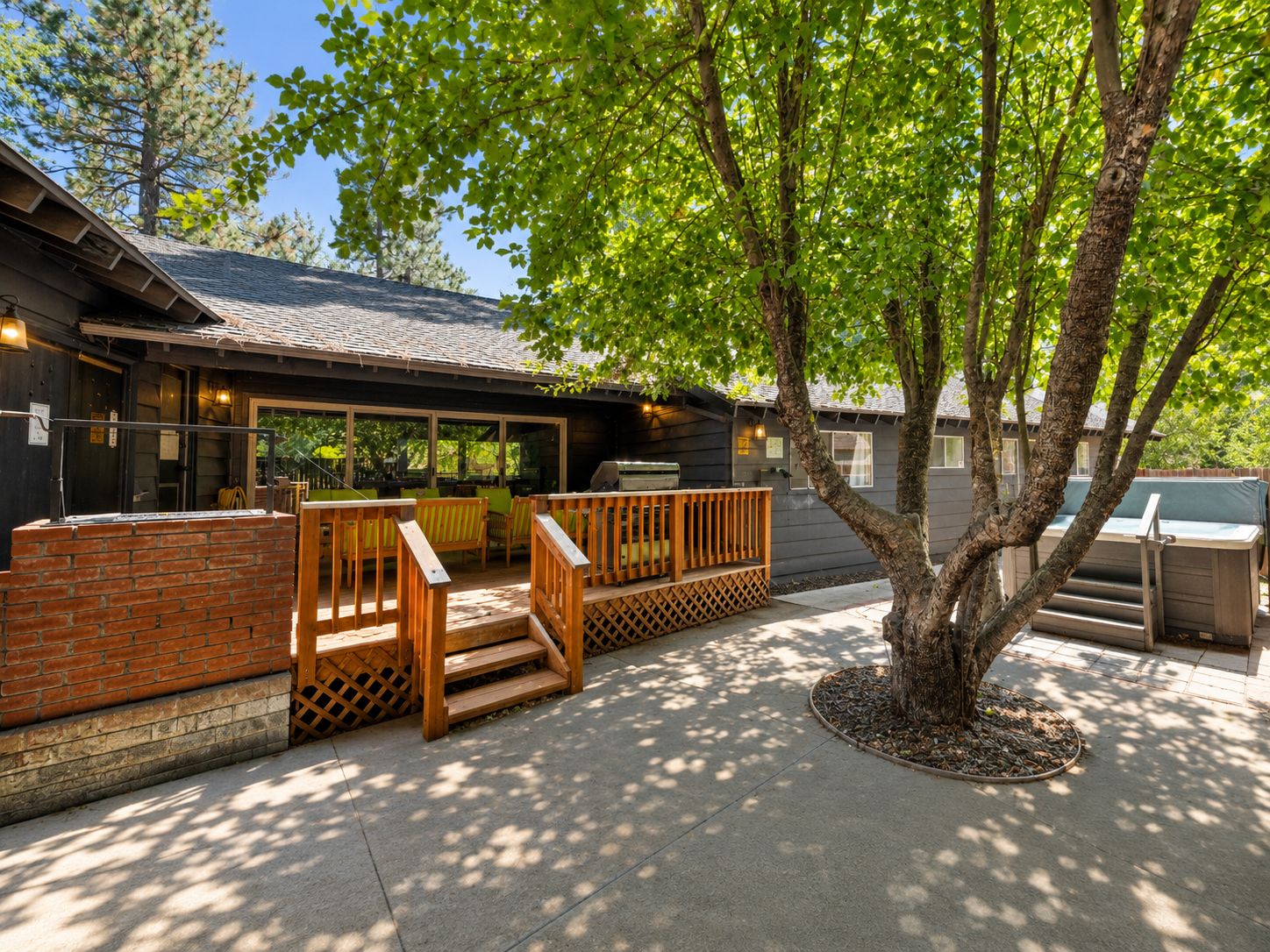 Un patio con mobiliario exterior, una parrilla y un árbol que da sombra.