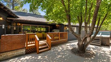 Un patio con mobiliario exterior, una parrilla y un árbol que da sombra.