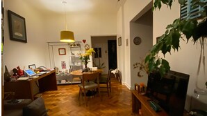 A living room with a wooden floor, a dining table with chairs, a TV on a wooden stand, and a hanging plant. - Charming and peaceful Santa Teresa (Santa Teresa Rio de Janeiro)