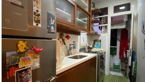 A compact kitchen with a refrigerator, microwave, and sink. There are wooden cabinets and a patterned floor. - Charming and peaceful Santa Teresa (Santa Teresa Rio de Janeiro)