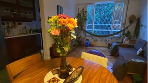 A dining area with a wooden table, a vase of flowers, and a hammock in the background. - Charming and peaceful Santa Teresa (Santa Teresa Rio de Janeiro)