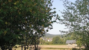 Two Adirondack chairs on a wooden deck with a view of a rural landscape.