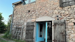 A stone building with a blue door and wooden shutters, a sign reading "Martin Pêcheur," and a lantern on the wall.