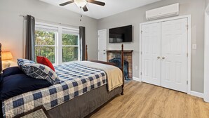 Een slaapkamer met een bed, een plafondventilator, een open haard en een aan de muur bevestigde televisie.