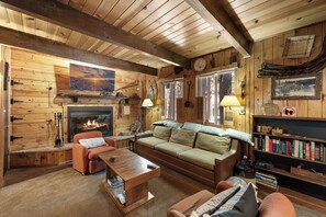 A cozy cabin interior with a fireplace, wooden furniture, and a bookshelf. - Gallagher's West (Big Bear Lake)
