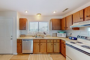 Compact kitchen with a gas stove, microwave, and dishwasher, featuring a window with blinds and a sink.