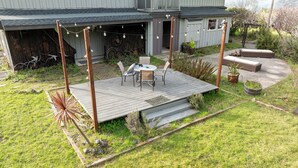 Um deck de madeira com mesa e cadeiras, cercado por um jardim com diversas plantas e um espaço de estar.