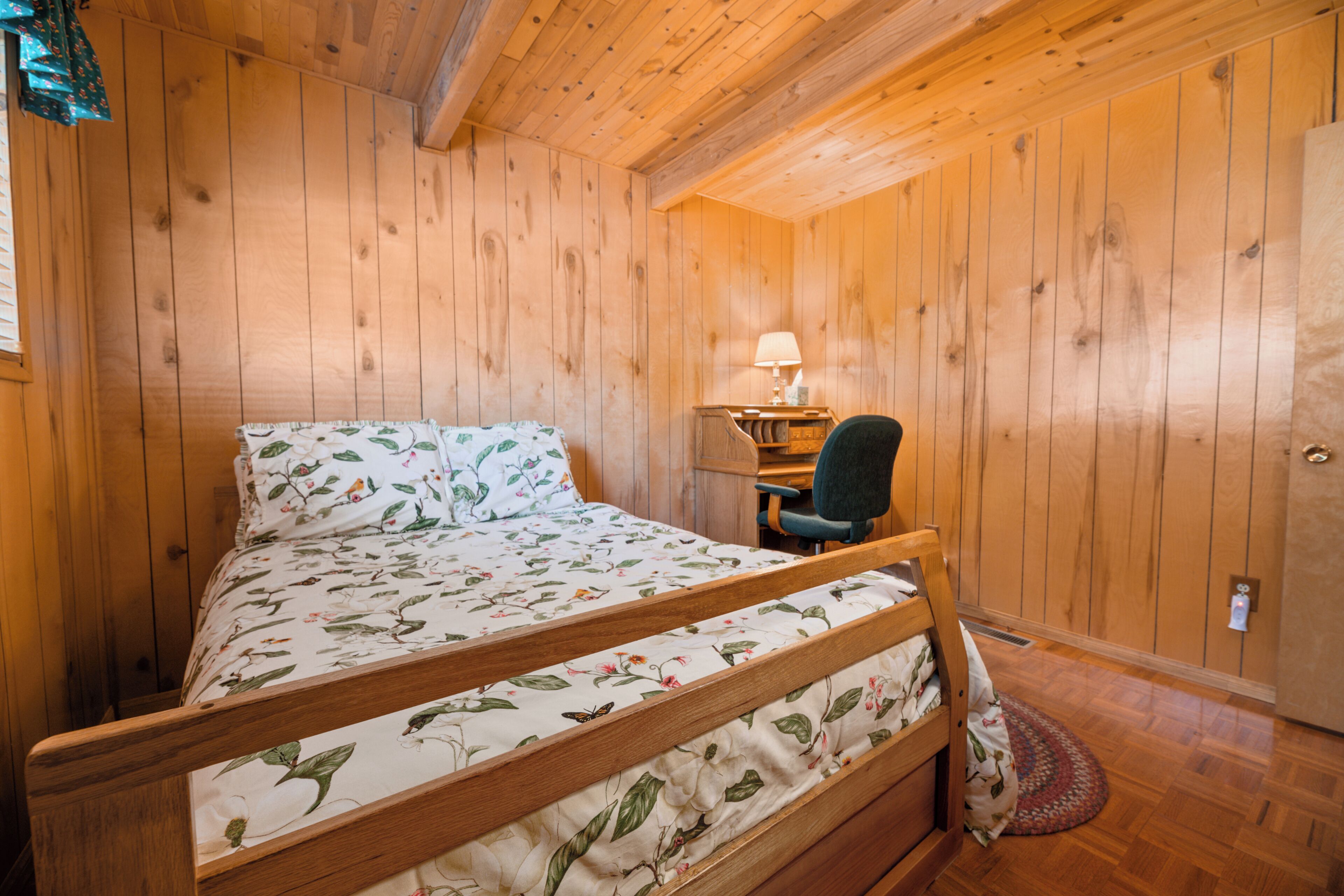 A wooden-paneled room with a bed, a desk, and a chair.