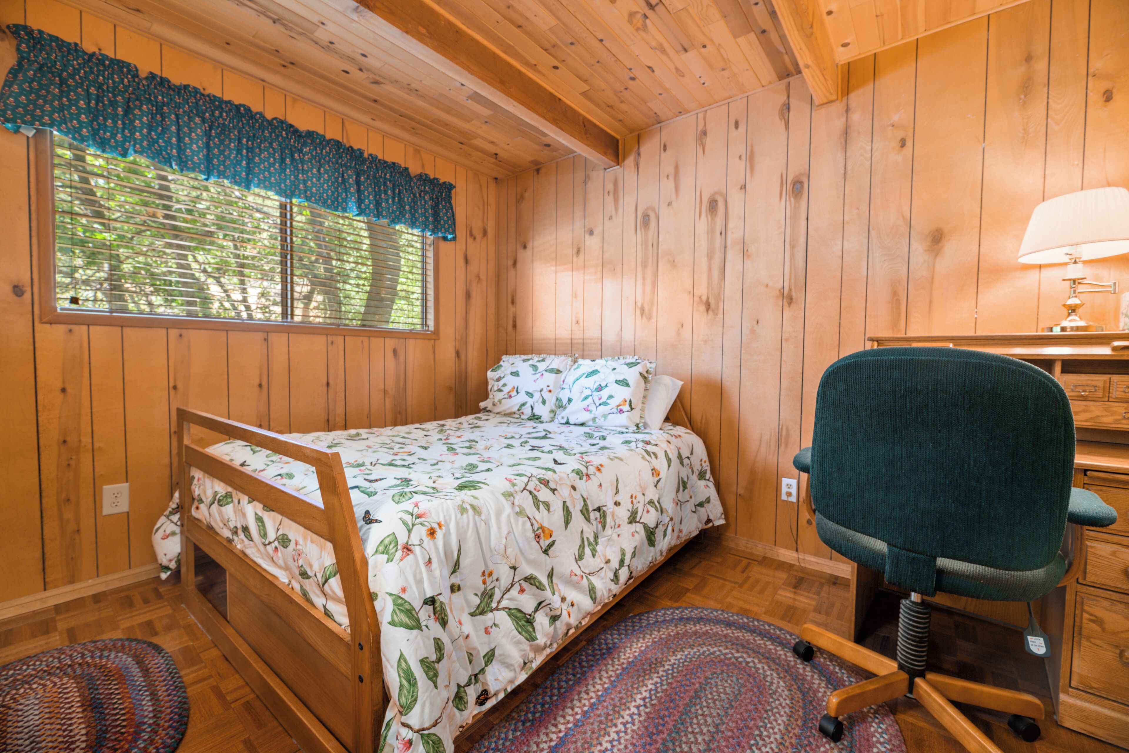 A wooden cabin bedroom with a bed, a desk, and a chair.