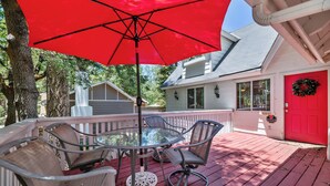 Une terrasse en bois rouge avec une table et des chaises en verre, un parasol rouge et une maison blanche avec une porte rouge.