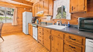 Une cuisine aménagée dans une cabane en bois, comprenant un réfrigérateur, une cuisinière, un évier et un lave-vaisselle.